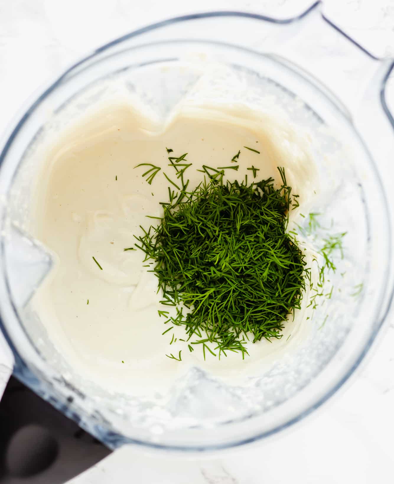 fresh dill on top of a creamy white sauce in a blender.