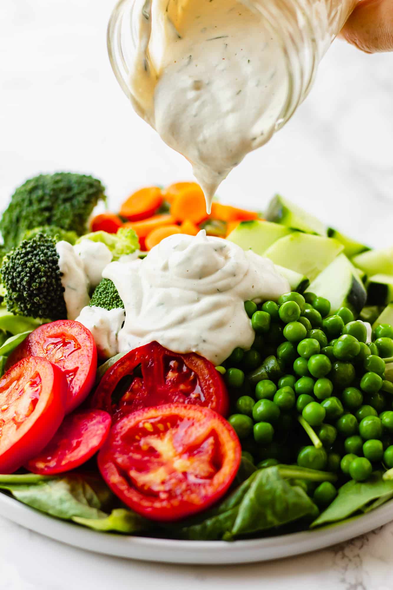 pouring vegan ranch dressing over a large green salad.