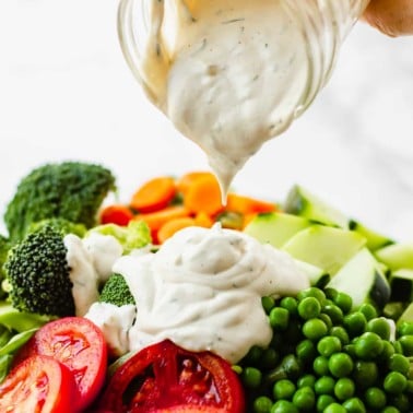 pouring vegan ranch dressing over a large green salad.