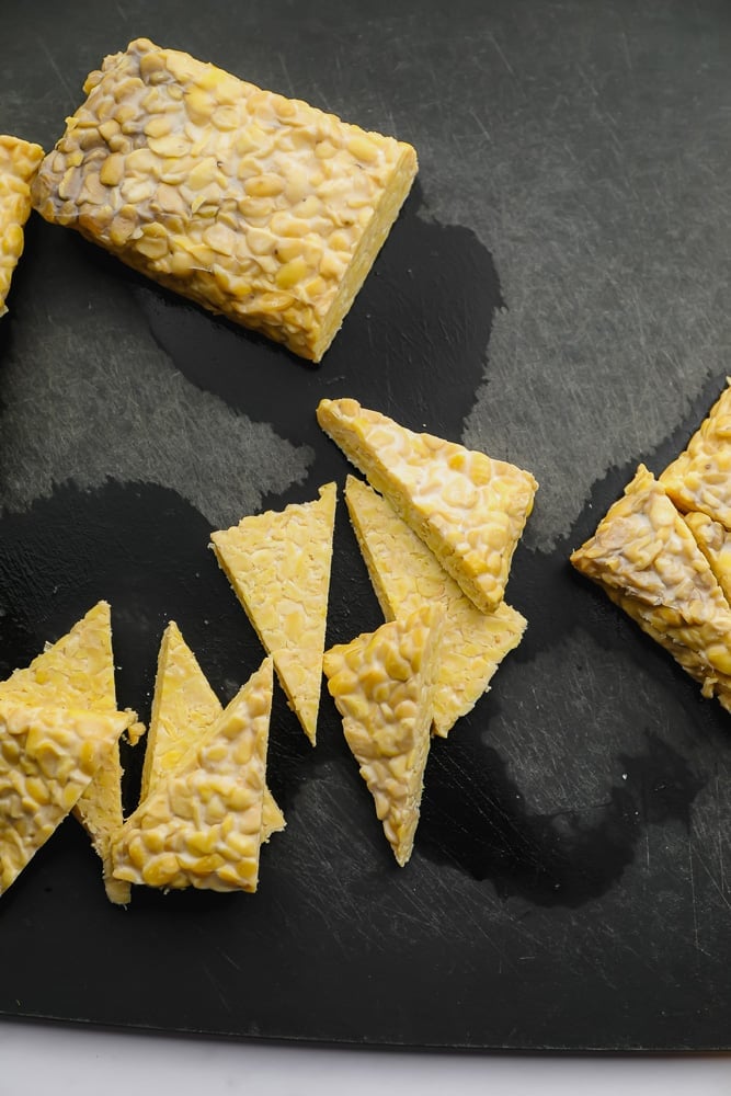 slicing tempeh into triangles on black cutting board