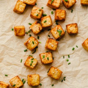 close up of air fryer tofu on parchment paper garnished with sesame seeds and chives.