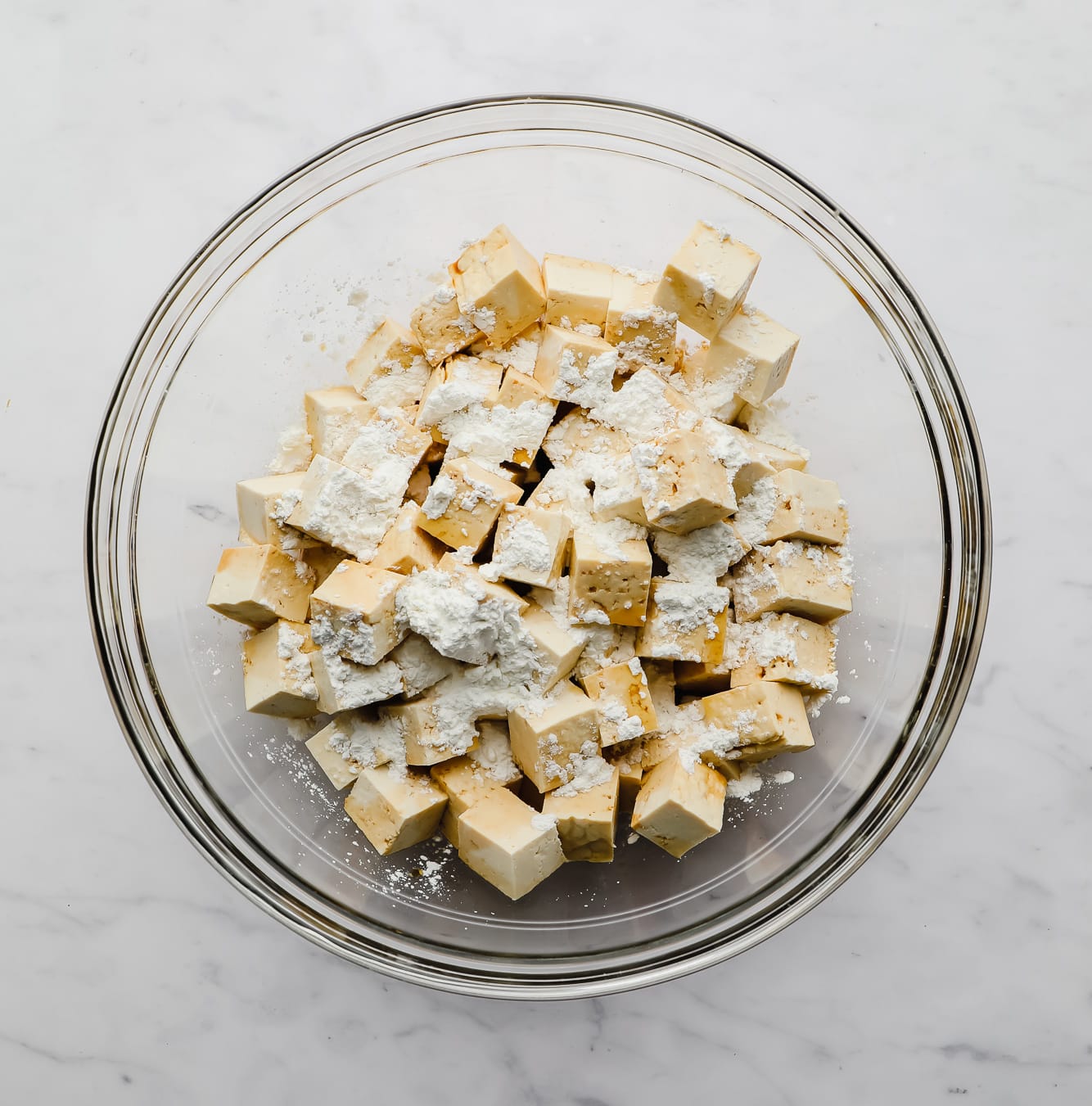 sprinkling cornstarch on top of tofu cubes in a large glass bowl.