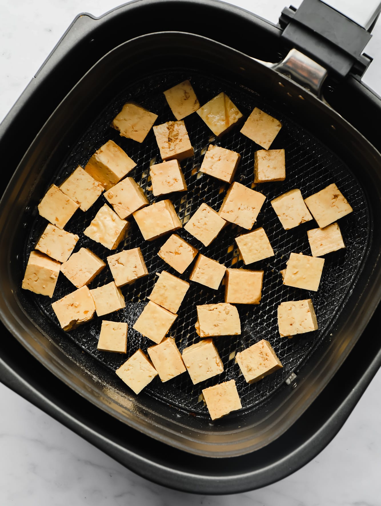 raw tofu cubes in an air fryer basket.