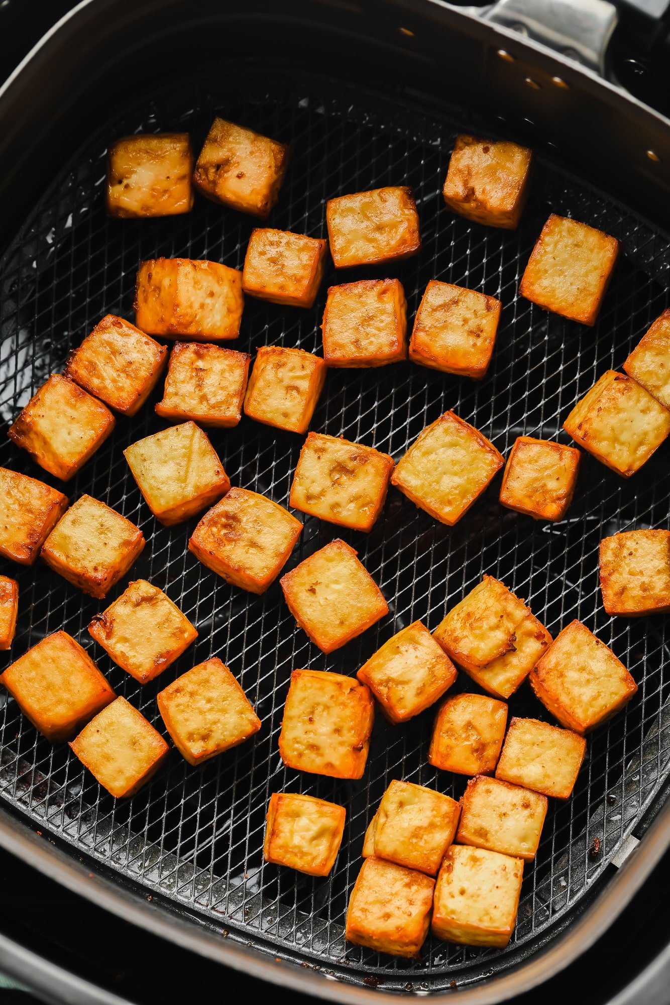 cooked tofu cubes in an air fryer basket.