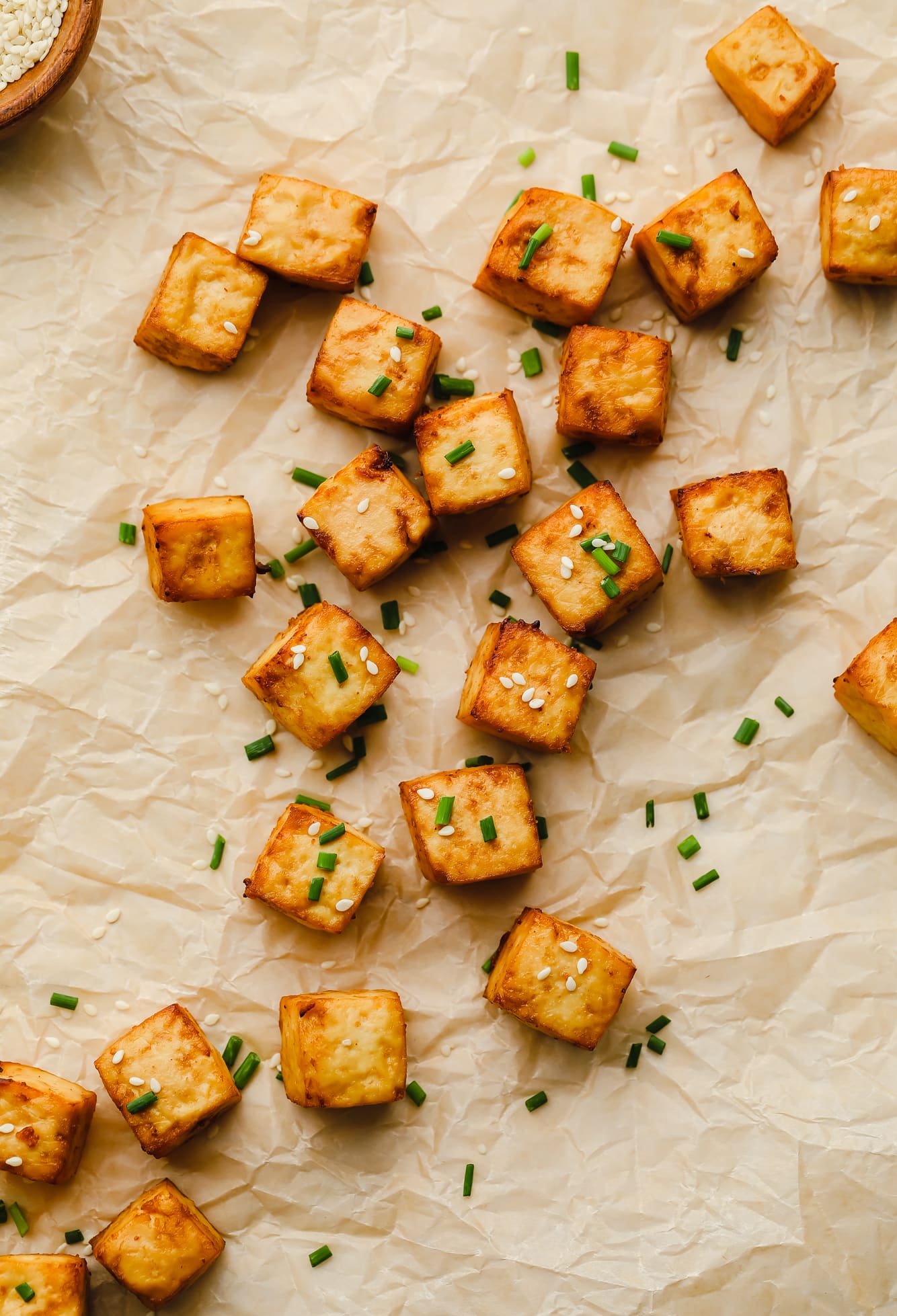 crispy air fryer tofu cubes garnished with sesame seeds and chives on a piece of parchment paper.