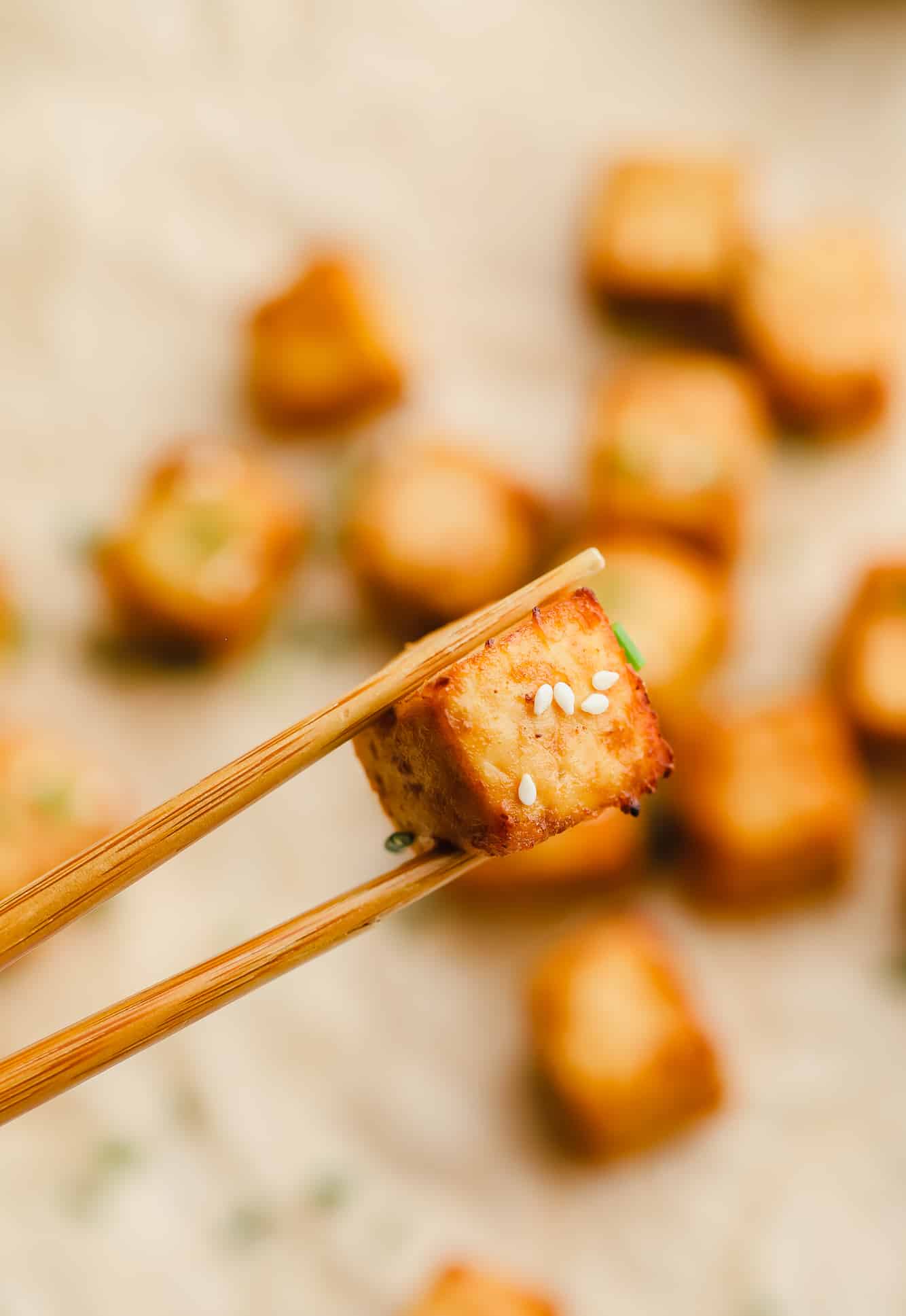 close up of an air fryer tofu cube being held up by wood chopsticks.