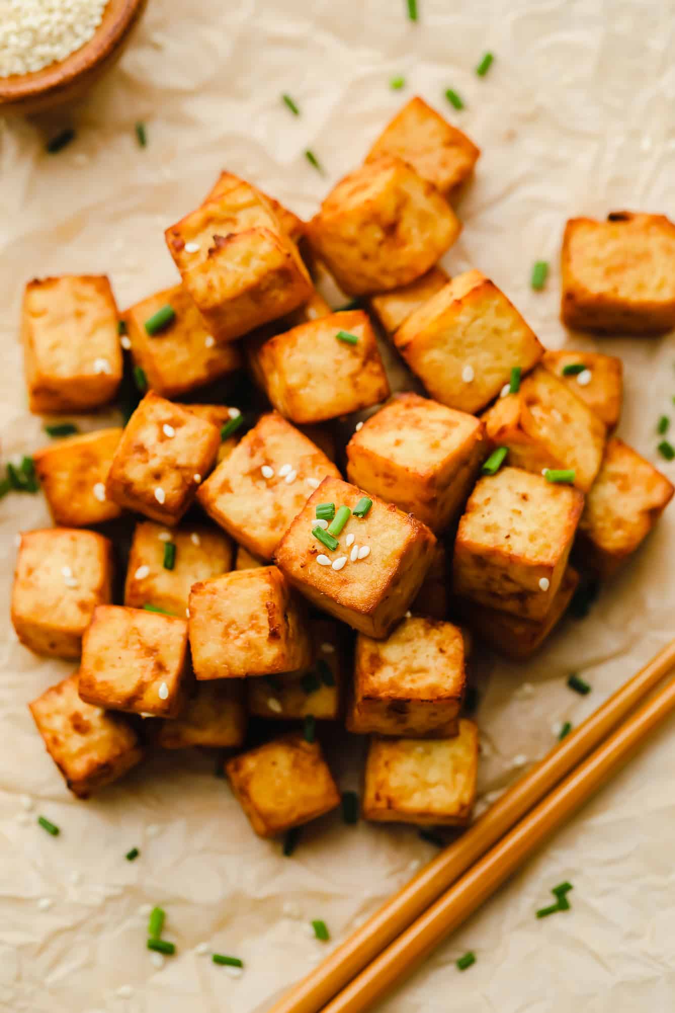 a pile of air fryer tofu garnished with sesame seeds and chives.