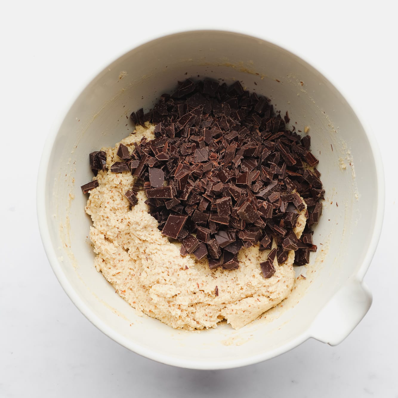 chopped chocolate on top of almond flour cookie dough in a large white bowl.