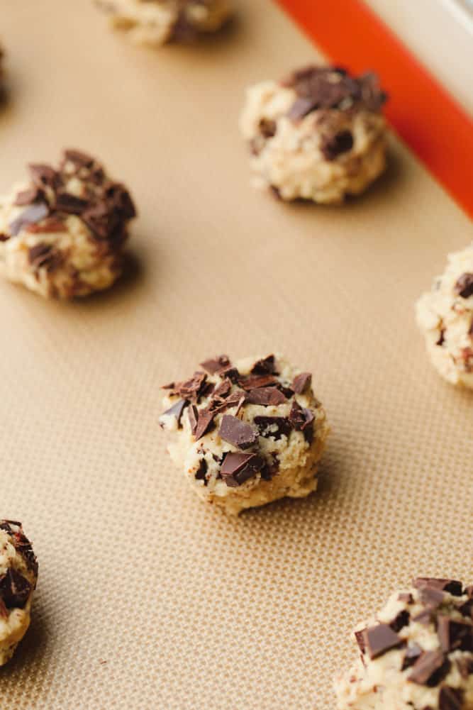 close up on raw chocolate chip cookie dough balls on a parchment-lined baking sheet.