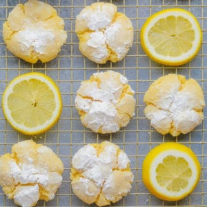 square image of several yellow cookies with powdered sugar and lemon slices on cooling rack