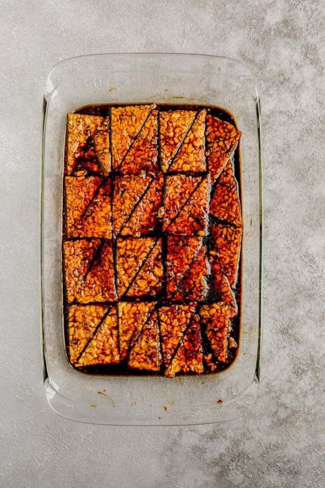 triangles of tempeh marinating in glass dish