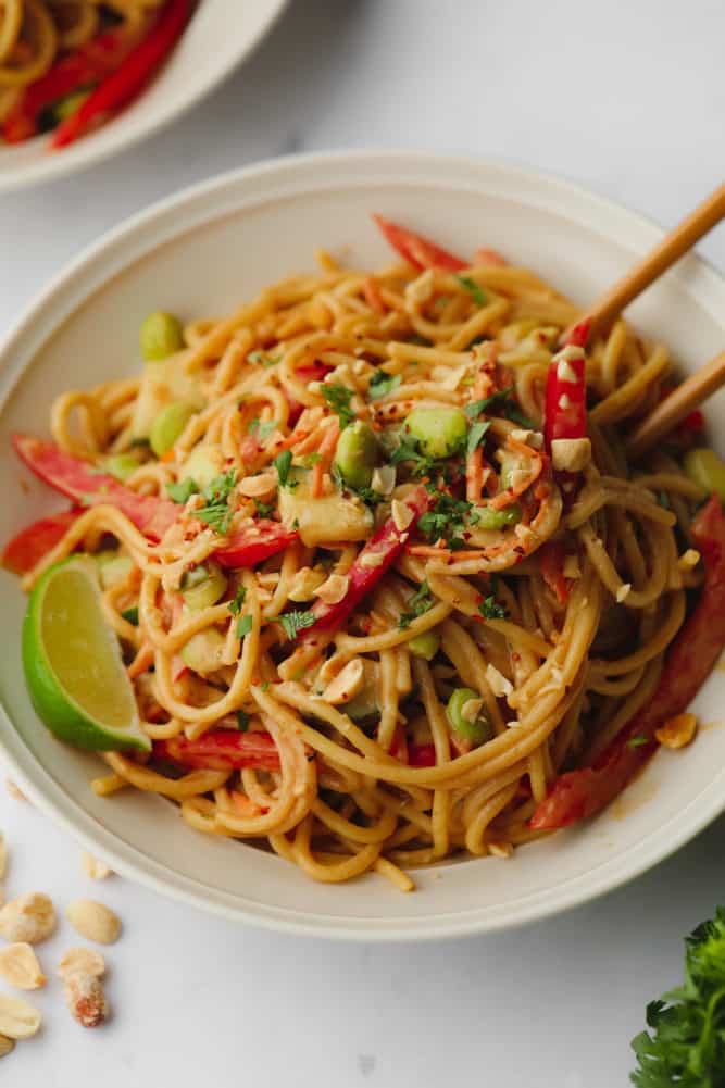 close up of a bowl of thai peanut noodles with chopsticks in bowl