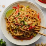 square image of a bowl with noodles and vegetables on white background