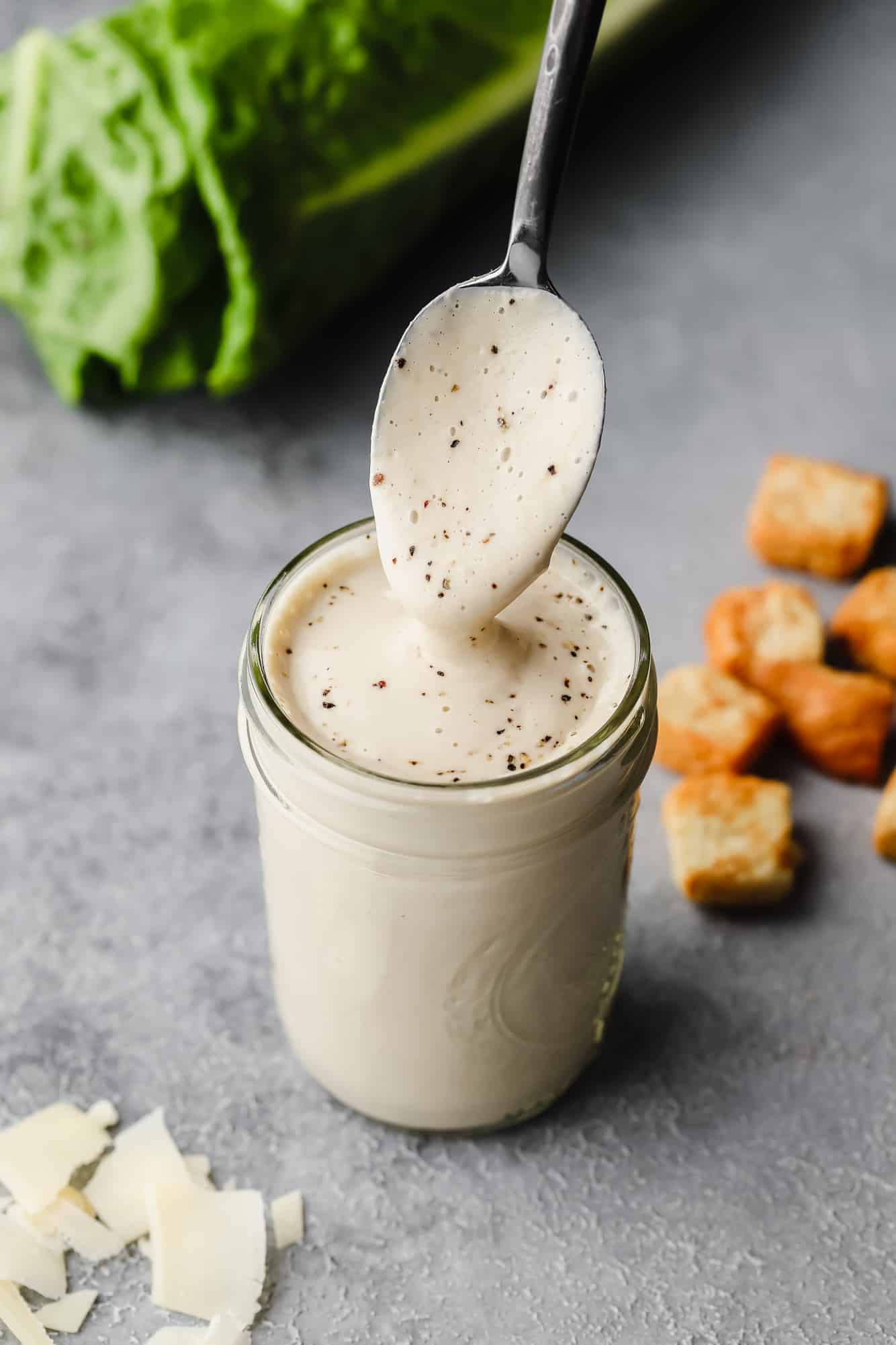 a caesar dressing-covered spoon lifting out of a jar filled with dressing.