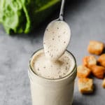 a caesar dressing-covered spoon lifting out of a jar filled with dressing.