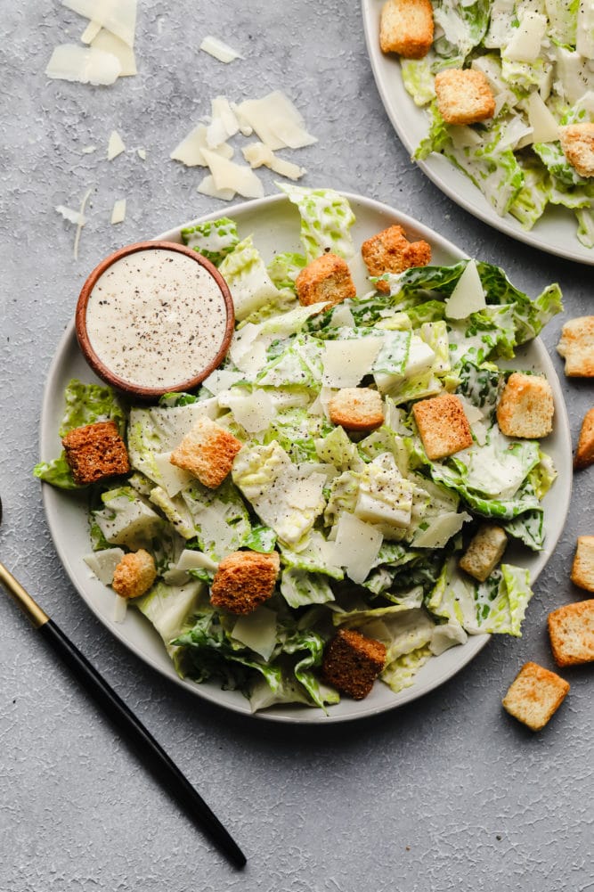 two plates of caesar salad on grey background