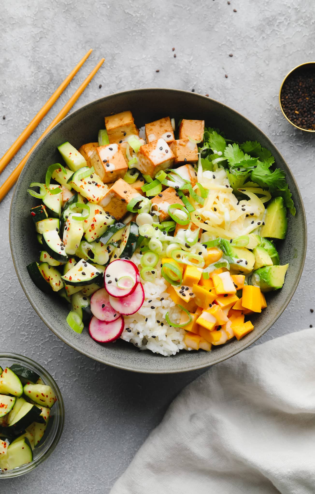 vegan poke bowl topped with mango, avocado, radishes, tofu, and cucumbers in a grey bowl.