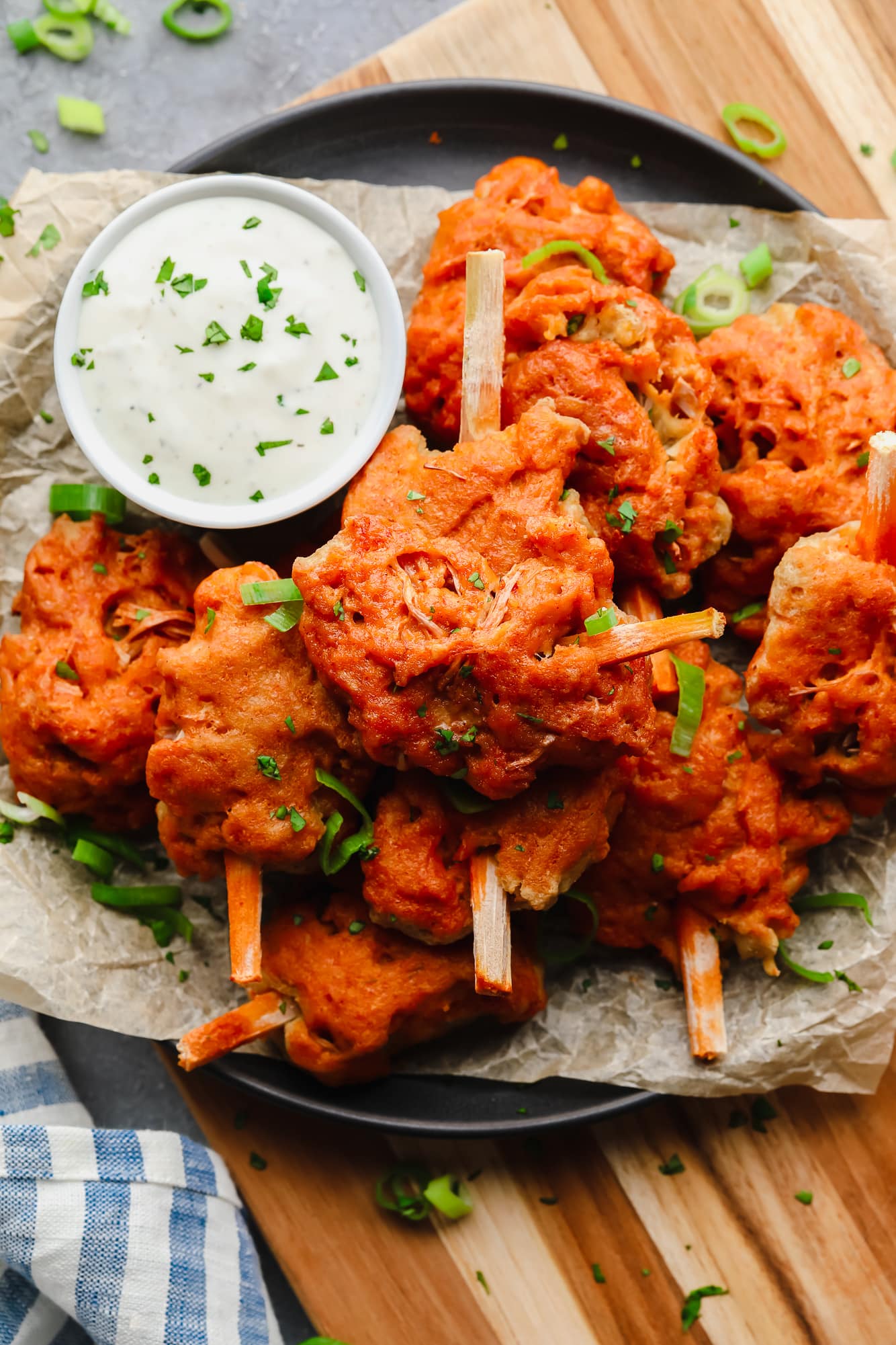 a pile of cooked vegan wings on a plate next to a small bowl filled with white dipping sauce.