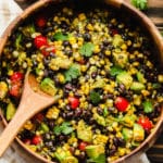 a wooden spoon scooping black bean salad out of a large bamboo bowl.