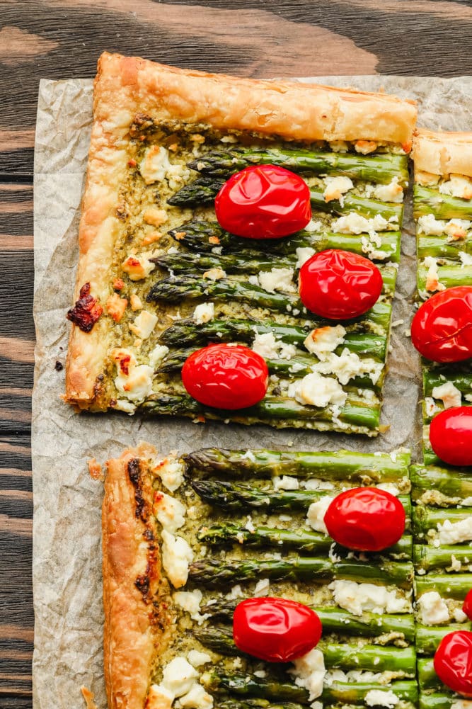 cut puff pastry tart with asparagus and tomatoes on wood background
