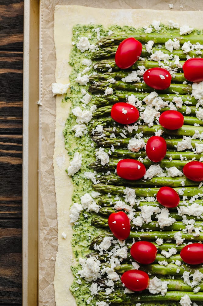 unbaked tart with peso, asparagus, tomatoes and feta on pan