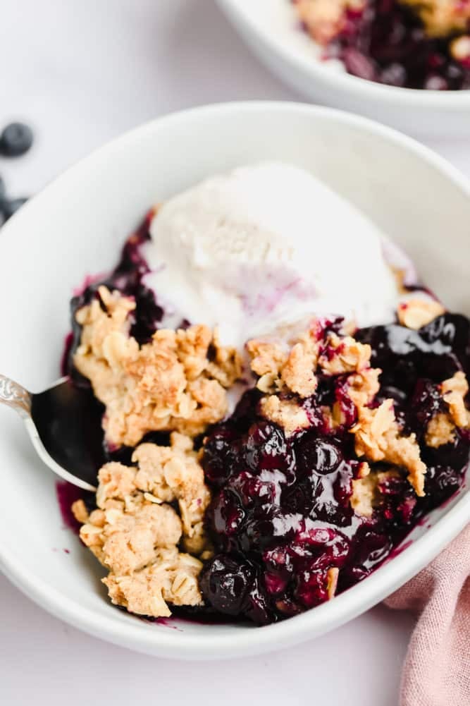 cooked blueberry crisp with ice cream in white bowl