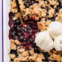 white casserole dish with blueberries and oat topping and vanilla ice cream
