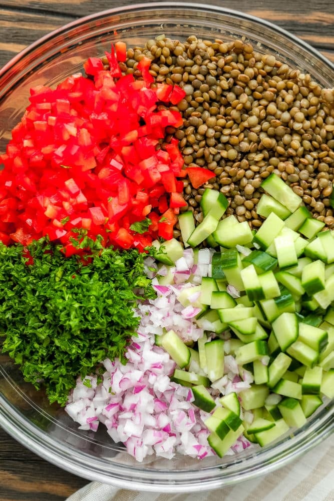 lentils, red peppers, parsley, red onion and cucumbers in a glass bowl