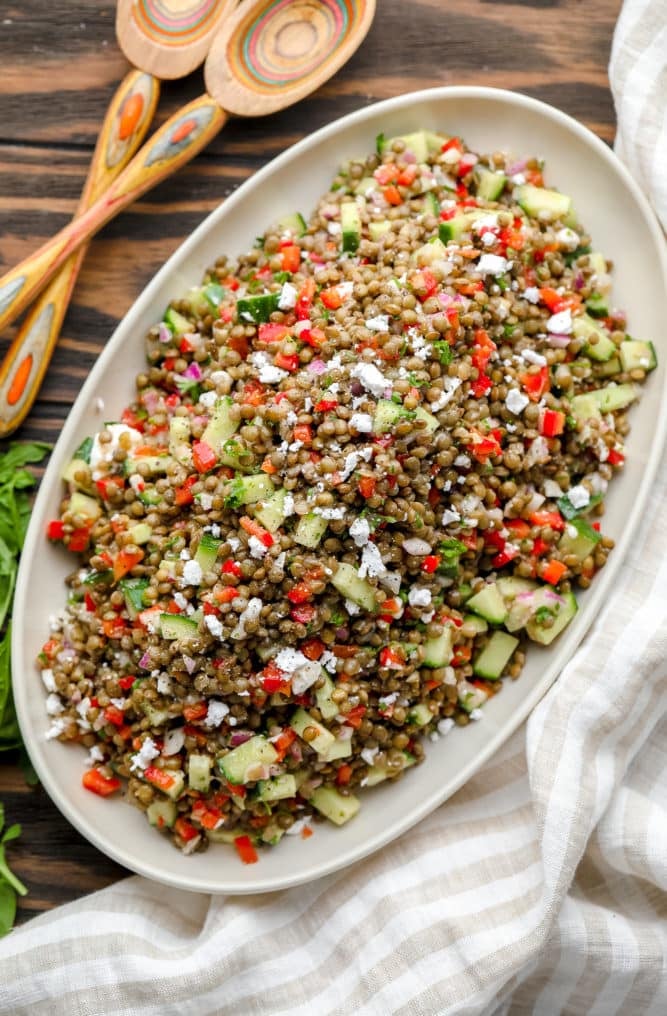 oval serving platter filled with lentil salad with cucumbers and red peppers, wooden background