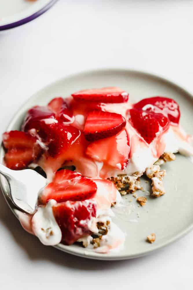 fork taking a bite of strawberry pretzel salad dessert on grey plate