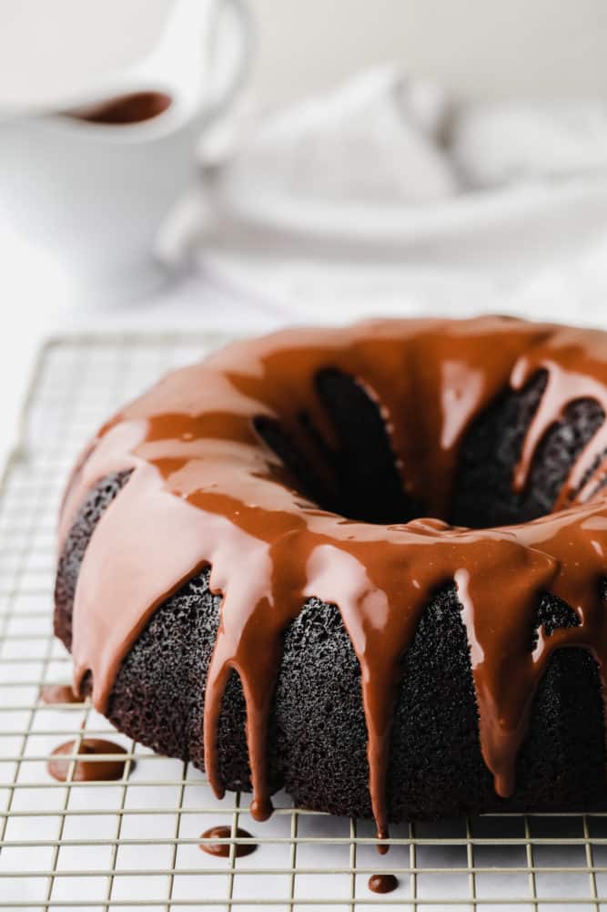 cooling rack with a chocolate cake and ganache drizzled, white background