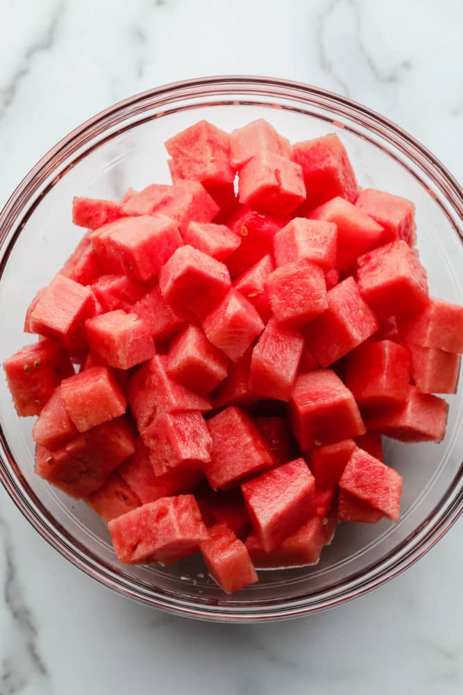 glass bowl of cubed watermelon on marble backdrop