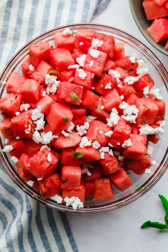 two bowls of watermelon with cheese and mint on marble backdrop