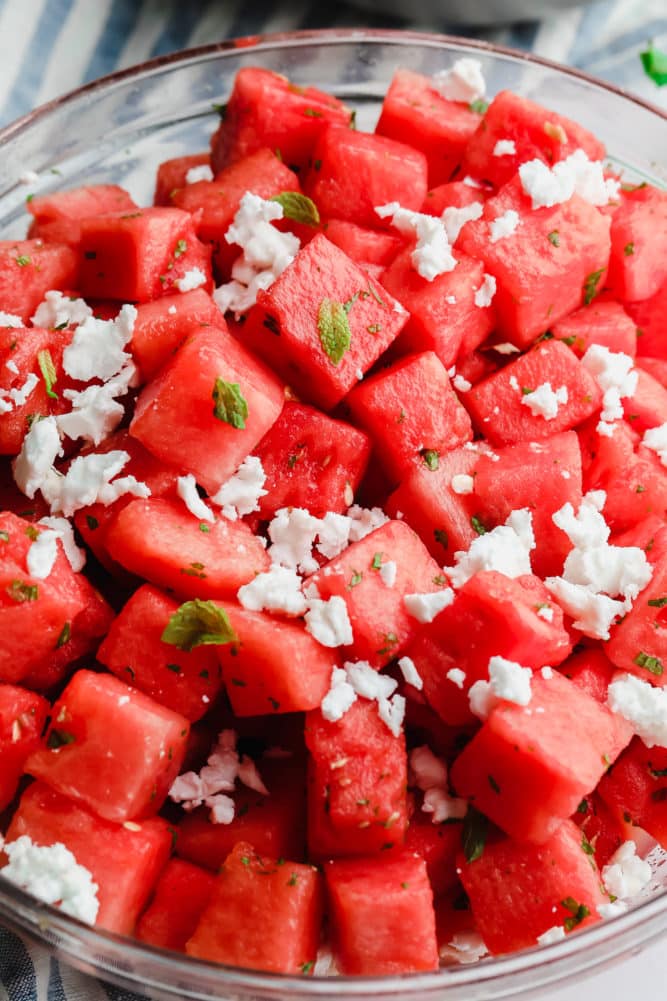 glass bowl of watermelon salad with feta and blue striped towel