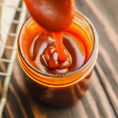 glass jar with caramel sauce drizzling into it from a spoon.