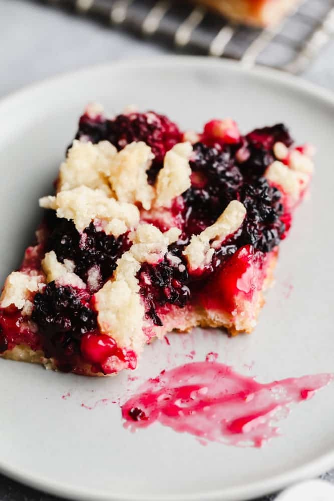 close up of a bar with blackberries and crumbly topping, bite taken out on grey plate