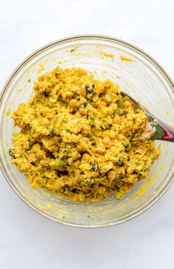 a colorful spoon mixing up chickpeas and other ingredients in a glass bowl