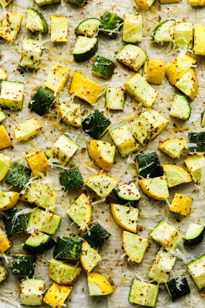 lots of roasted chunks of squash and zucchini on parchment lined pan with cheese on top