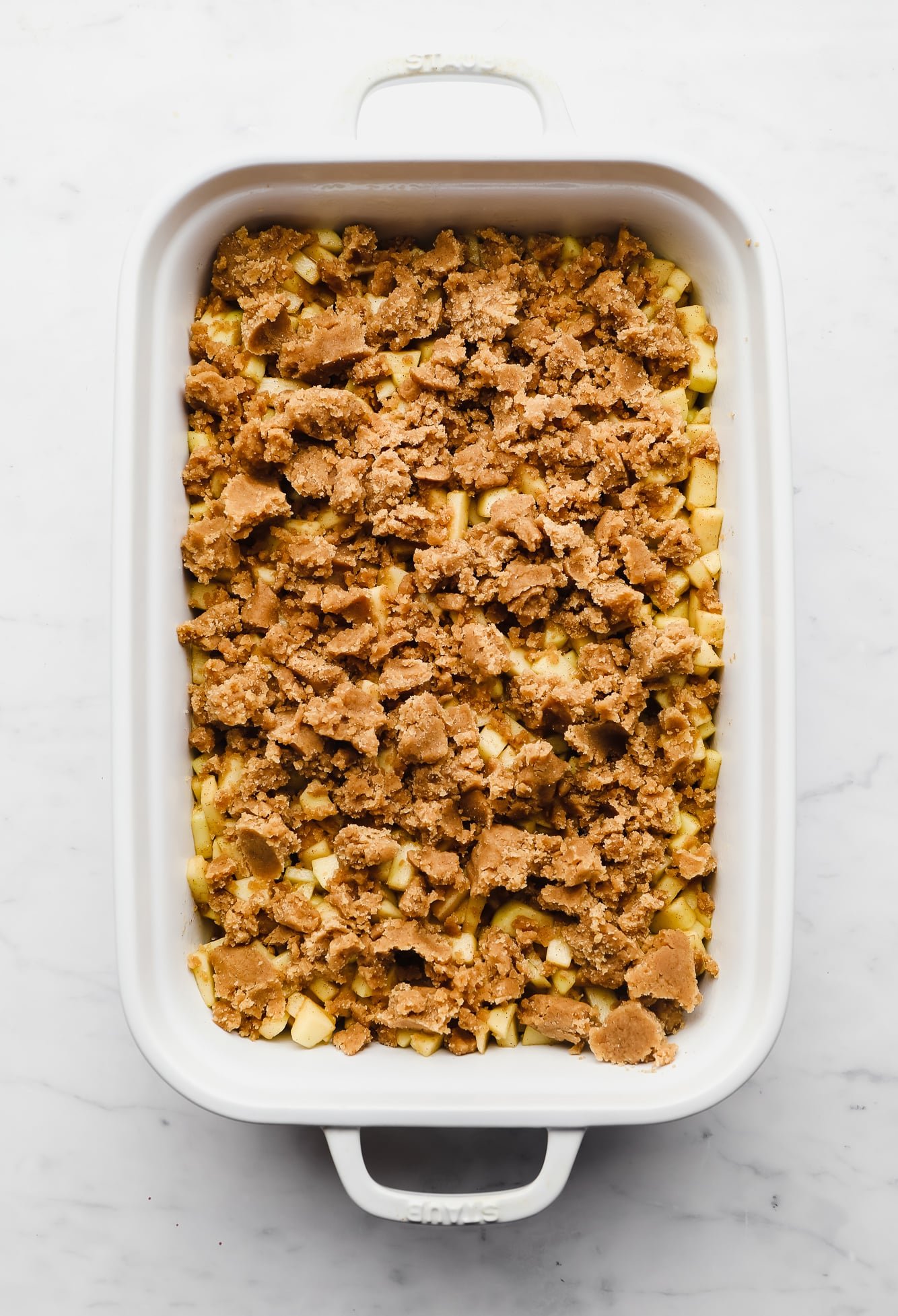 an unbaked apple crumble in a large white casserole dish.