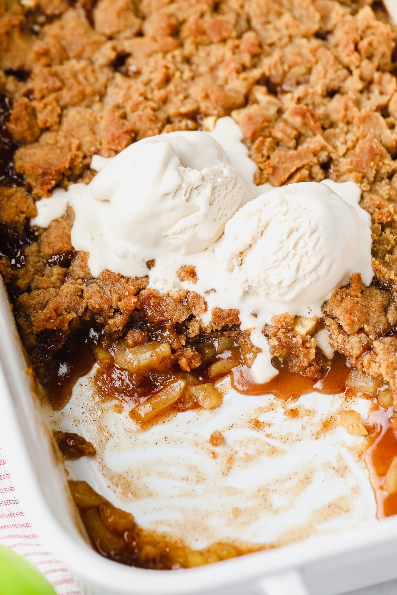 close up on vegan apple crumble in a casserole dish with a scoop missing and vanilla ice cream on top.