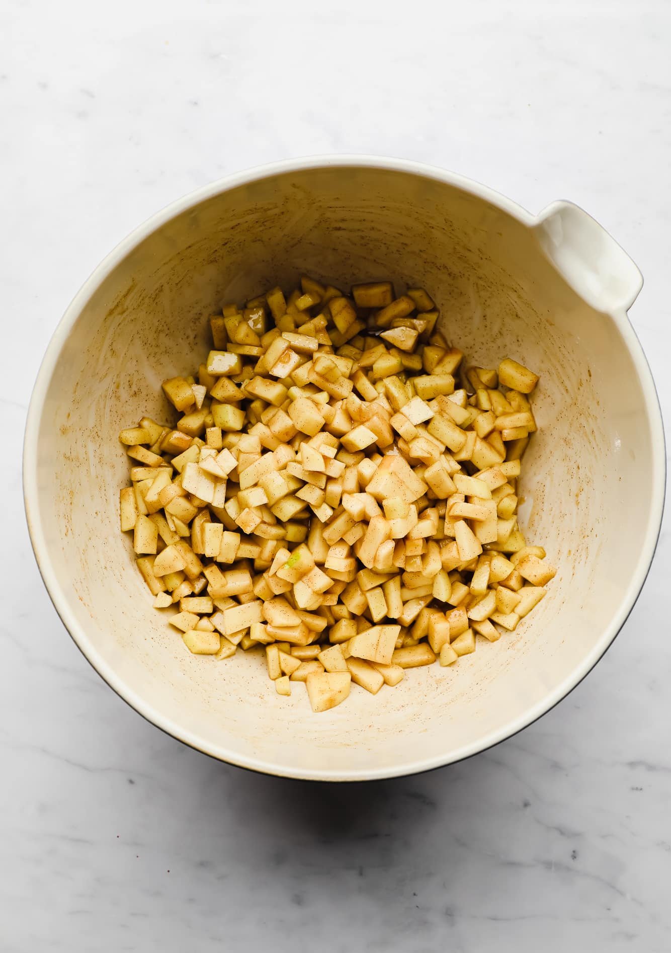 apple chunks coated in cinnamon in a large white bowl.