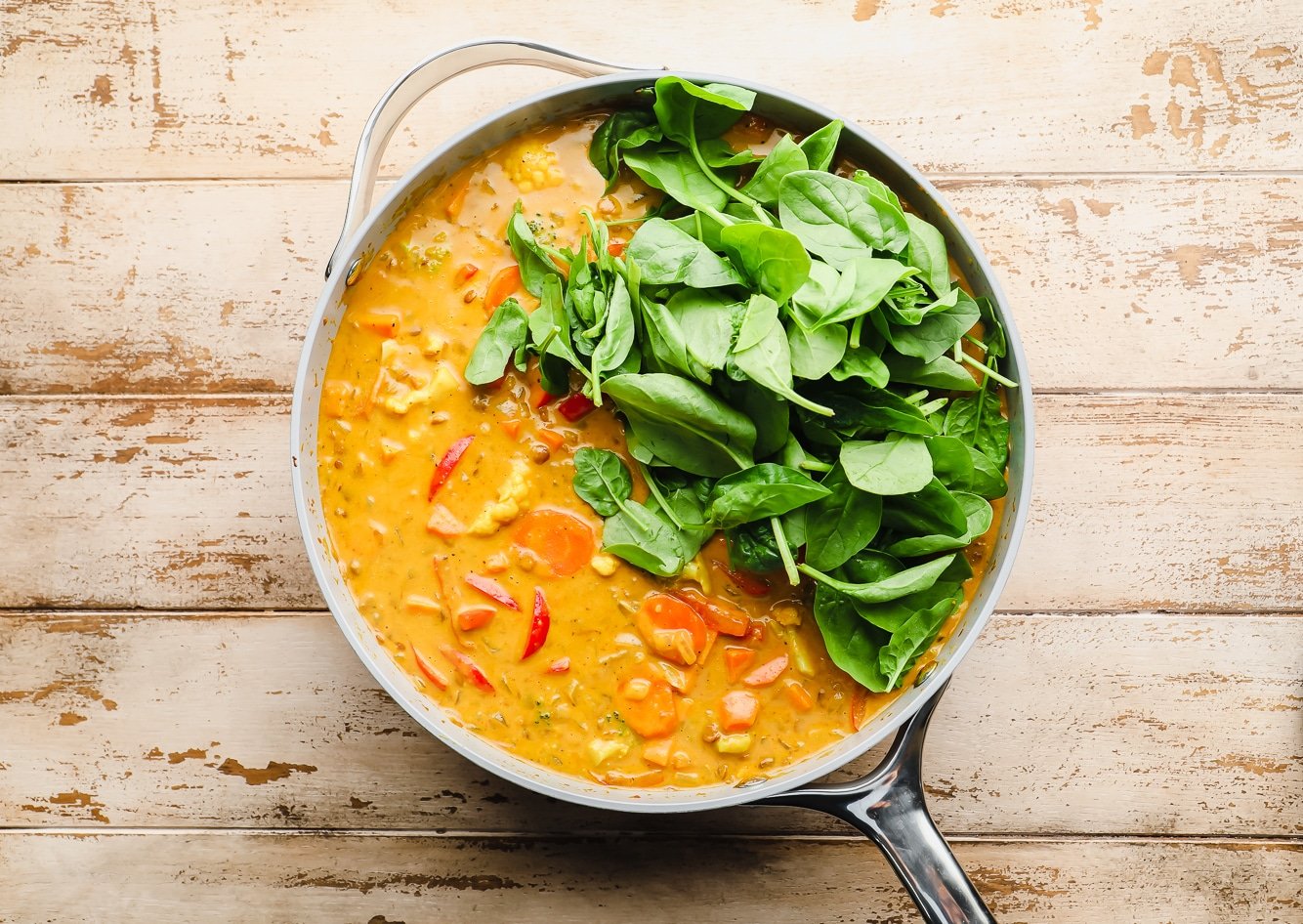 fresh spinach on top of a batch of vegan curry in a large grey pot.