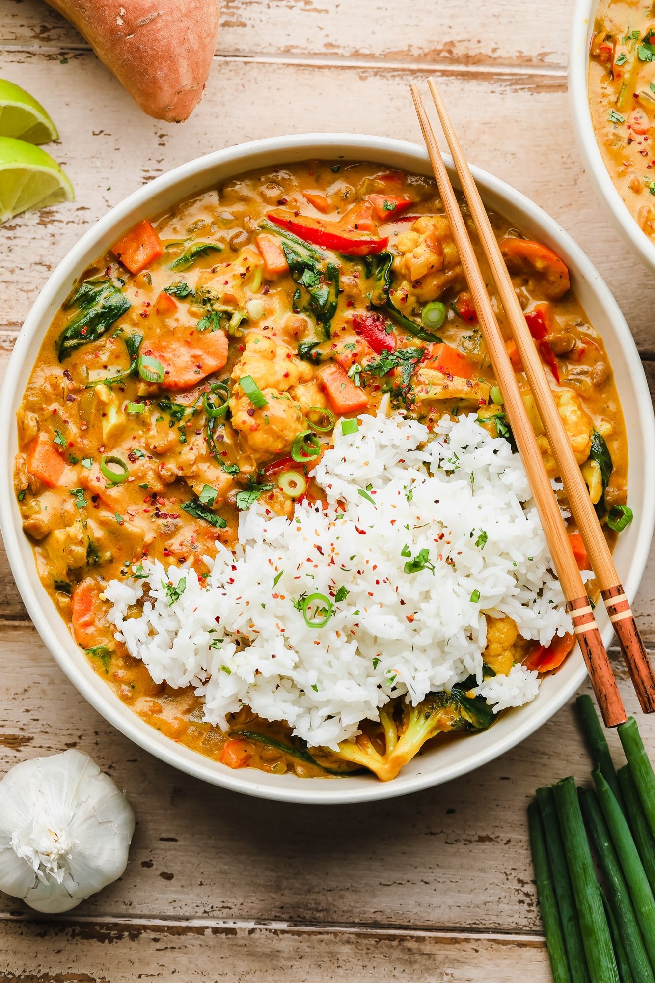 A white bowl filled with vegan curry and basmati rice. Wooden chopsticks sit on top of the bowl.