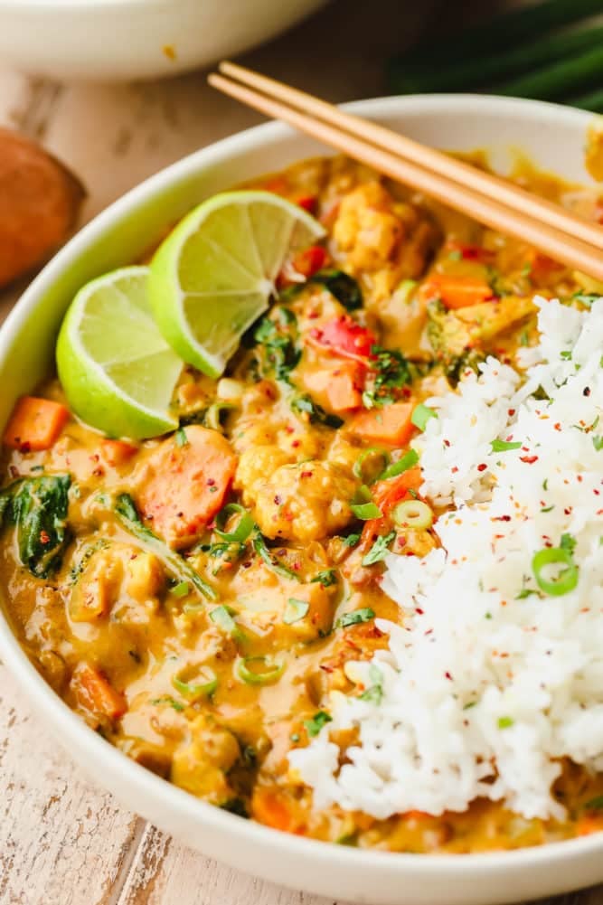 close up on a bowl of vegan curry with white rice, lime wedges, and chopsticks.