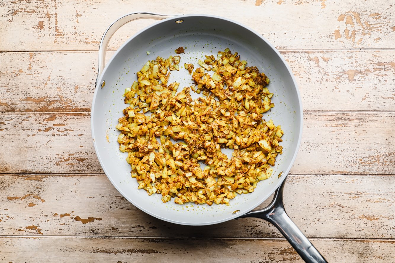 Sauteeing onions with curry powder in a large grey pot.