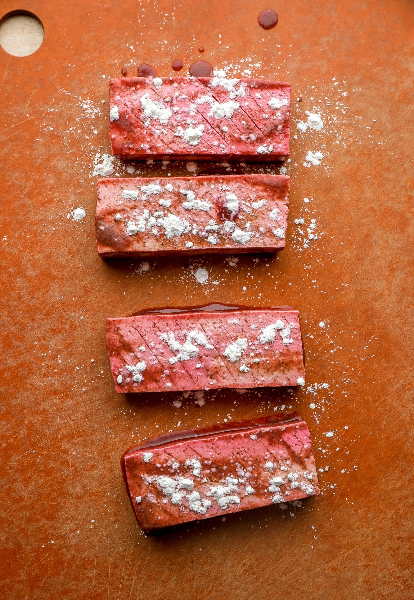 4 pieces of vegan salmon with cornstarch sprinkled on top on a red cutting board.