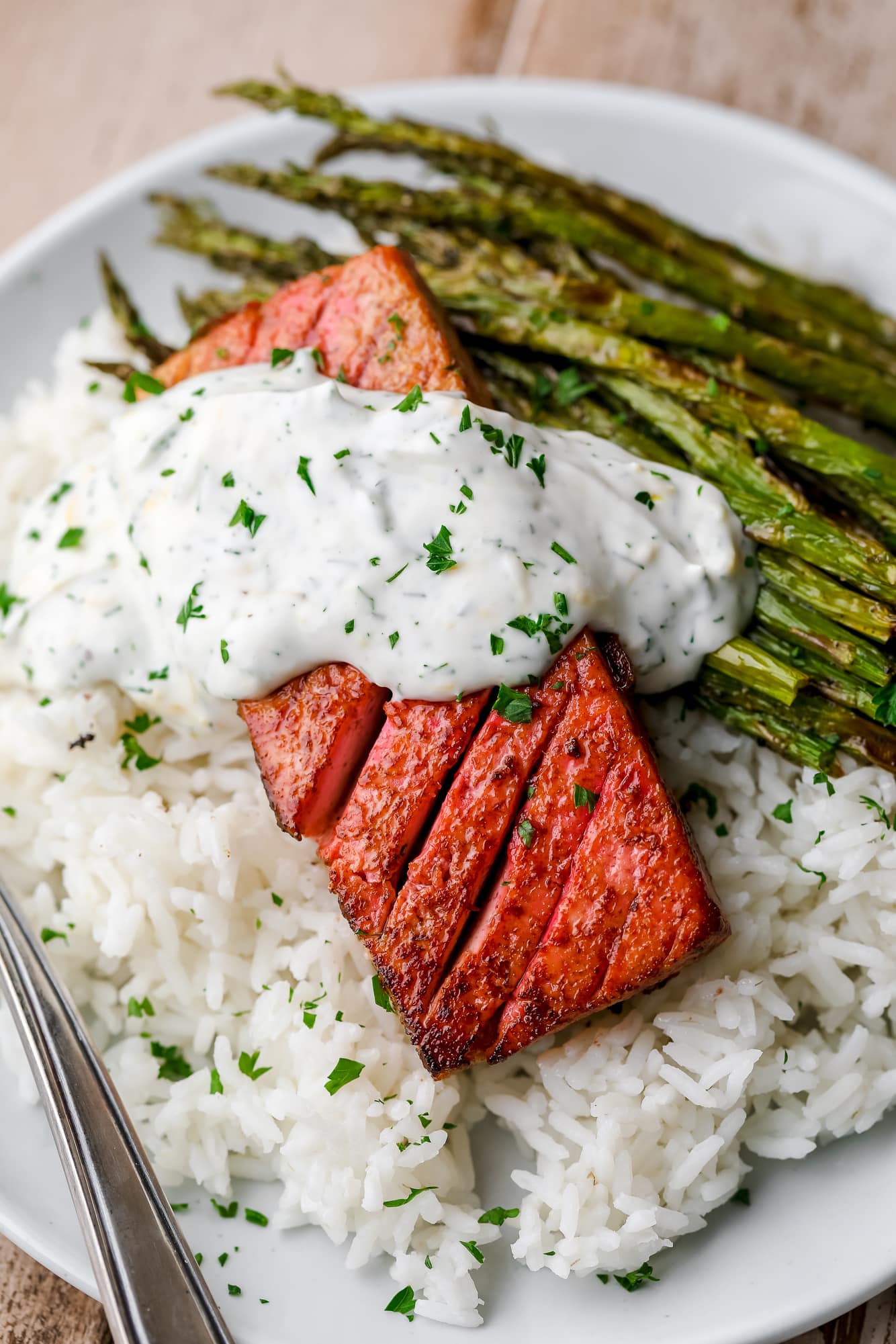 close up on a piece of vegan salmon on a bed of rice and asparagus on a white plate.