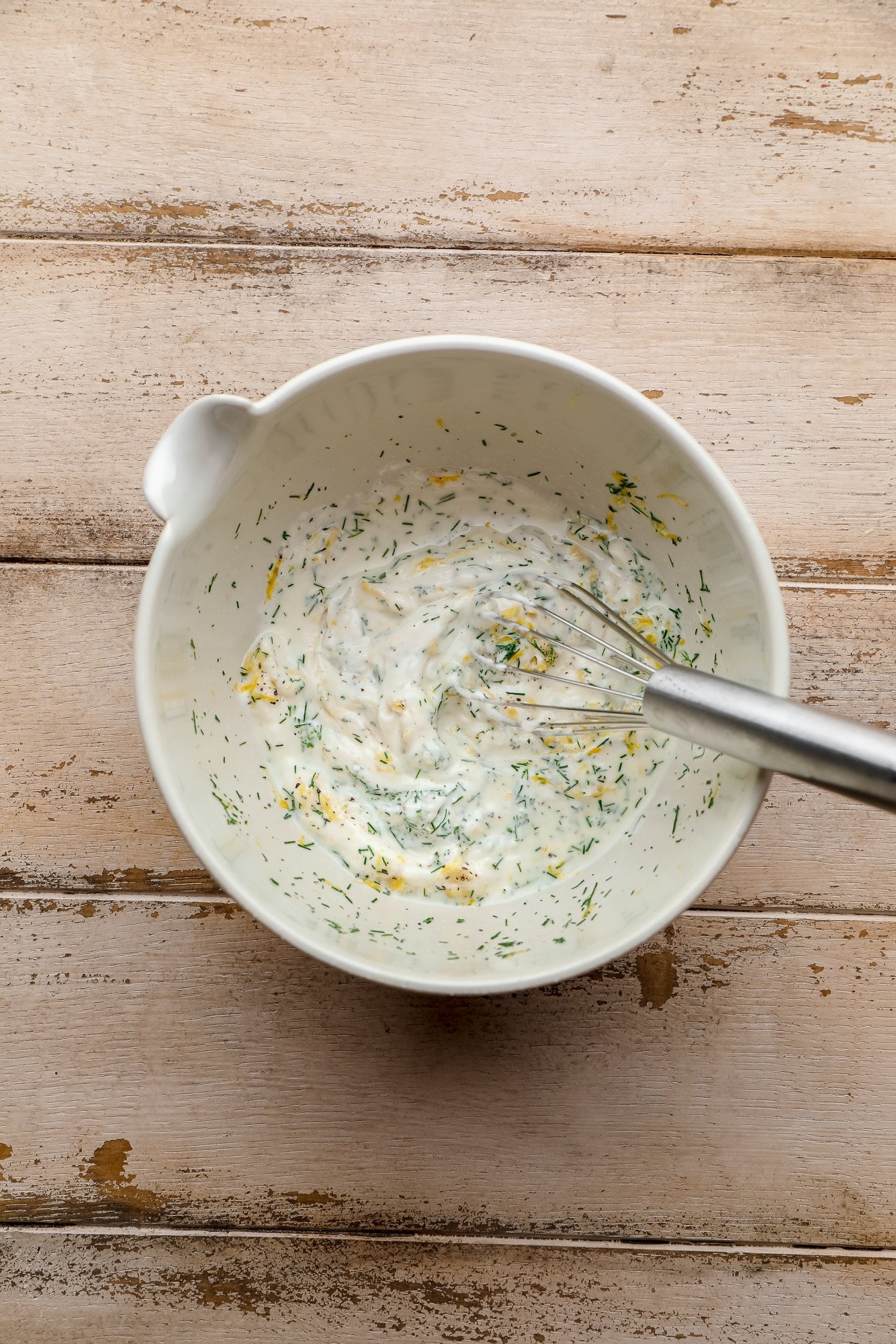 whisking lemon dill sauce ingredients together in a white bowl.