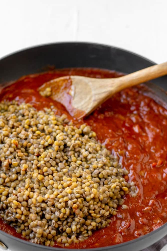 lentils being mixed into a tomato sauce in pan