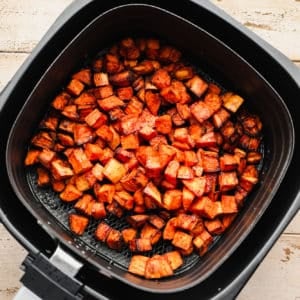 black air fryer with cooked sweet potato chunks in it.